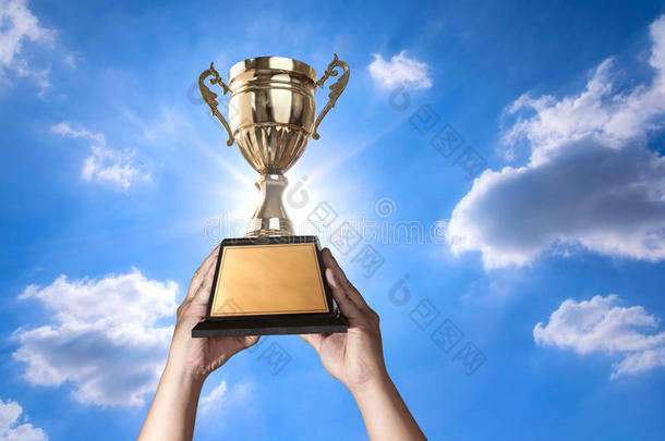 一个男人举着一个金色奖杯，上面有天空和太阳的腮红背景，为你的奖杯设计准备了复制空间。