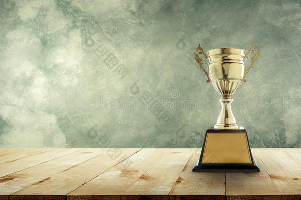 冠军黄金奖杯放置在一张木制桌子上，有复古的墙壁背景复制空间，为您的设计做好准备。