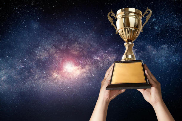 一个男人拿着一个金色的奖杯杯，有着银河系的天空背景