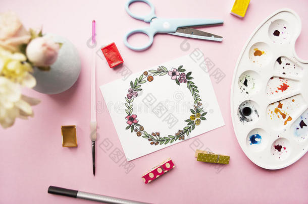艺术家工作空间。 花圈框架手绘水彩，菊花和玫瑰花束，眼镜，画笔，剪刀