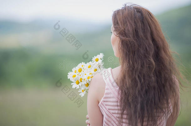 穿着粉红色无袖连衣裙的女孩带着一束洋甘菊