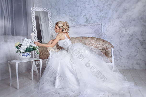美丽的新娘穿着婚纱，坐在沙发上，在一个白色的摄影棚里。