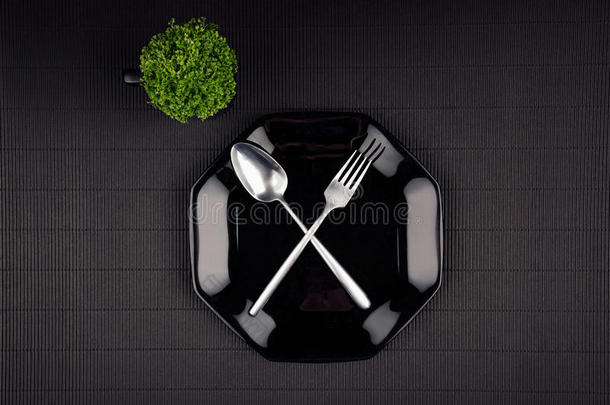 黑暗的现代简约餐厅菜单模拟黑色光滑的盘子，勺子，叉子和绿色植物，顶部视图。