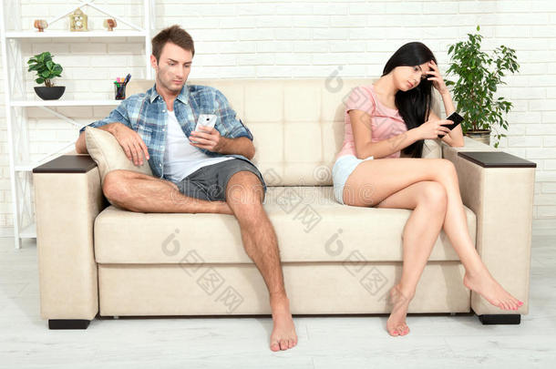 智能手机成瘾的概念照片。 年轻的女人和男人坐在沙发上，拿着智能手机，不看