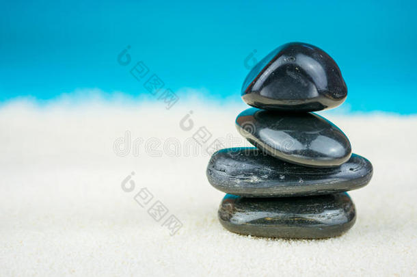 生长在明亮的沙子上的黑色鹅卵石，背景是蓝色的