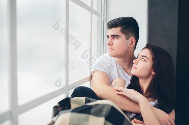 一对相爱的夫妇躺在阳光下的窗户旁。 明亮舒适的卧室。 家庭的安慰和爱