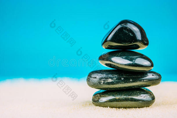 在明亮的沙子上堆积着四个黑色的鹅卵石，背景是蓝色的