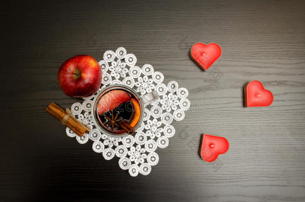 心形蜡烛，在花边餐巾、苹果和肉桂棒上用香料覆盖葡萄酒。 黑色的木头背景