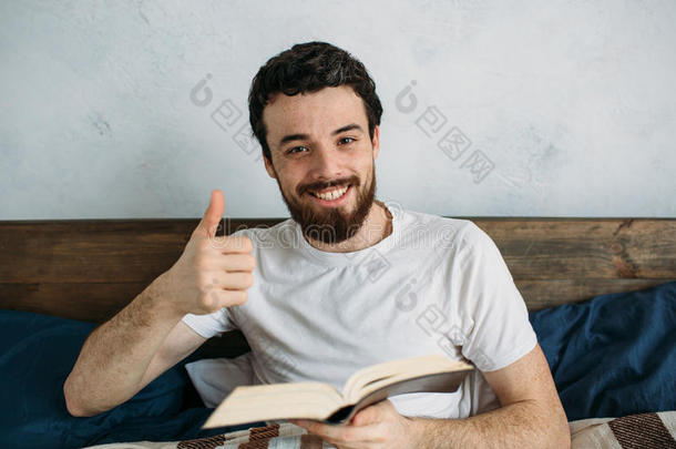 大胡子男人躺在卧室里读一本大书。