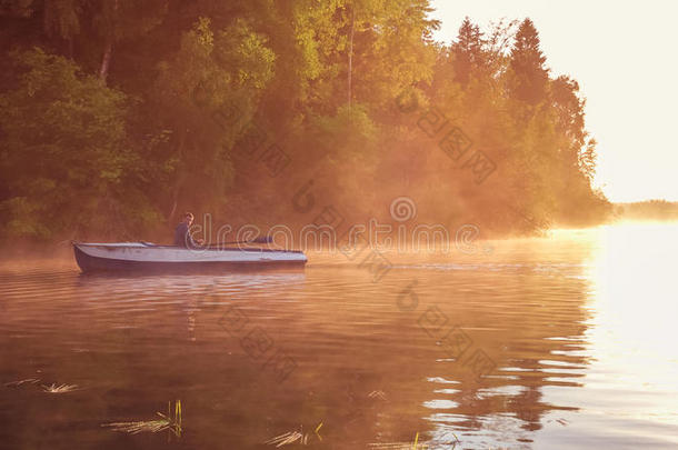 一个年轻人在金色的夕阳下骑着一艘船在湖上。 日落时的划船者。 与自然概念的统一