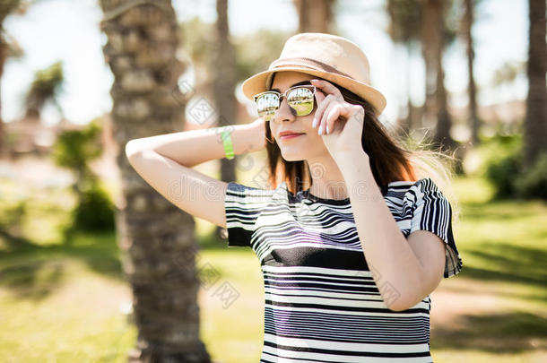 在夏天的女人戴着帽子和太阳镜，在夏天的手掌背景下。 暑假。