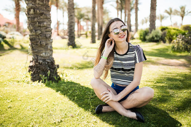 一个年轻的女人坐在草地上，在度假胜地享受夏日的阳光。 暑假