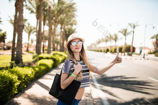 年轻漂亮的女孩把车停在棕榈树和马路上。暑假