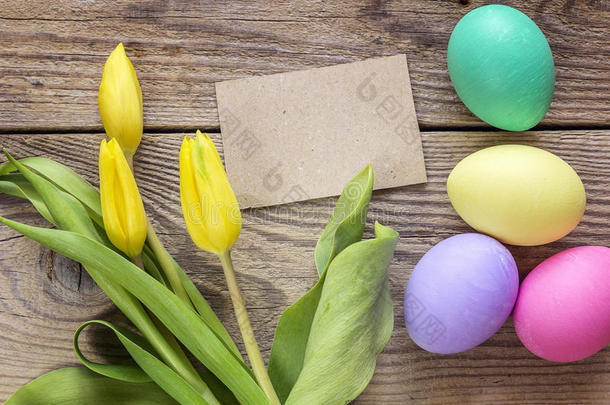 空的棕色卡片，复活节鸡蛋和郁金香在一张旧的木桌上。