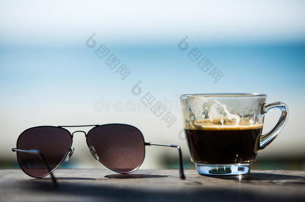 咖啡杯和太阳镜在木桌上与海滩椅子和沙子