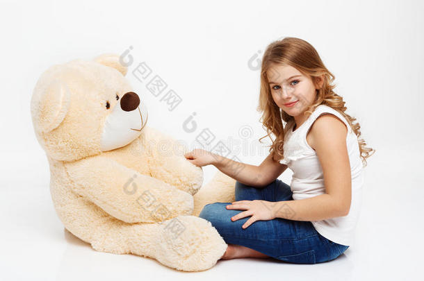 女孩坐在地板上，玩具熊拿着他的爪子。