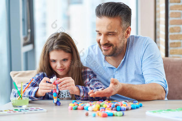 美丽的小女孩和她的父亲一起玩彩色布景来创造