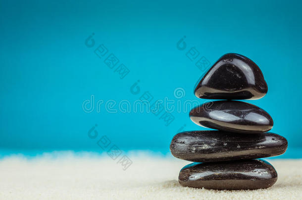 在明亮的沙子上堆积着四个黑色的鹅卵石，背景是蓝色的