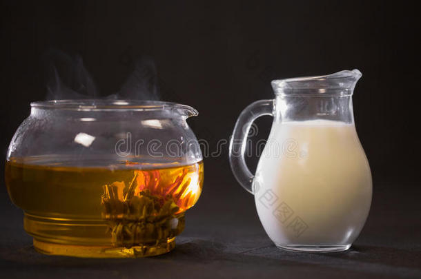 中国绿色盛开的茶芽在<strong>一个玻璃</strong>茶壶。 牛奶在b上的<strong>一个小</strong>罐子里