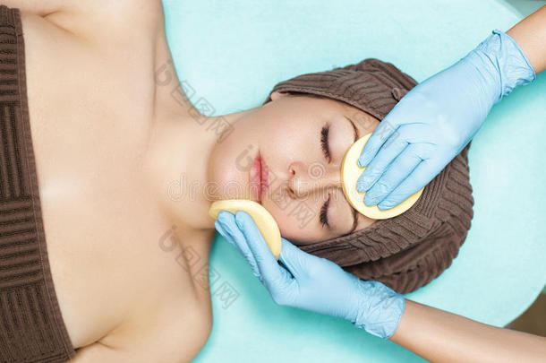 医生美容师用海绵清洁皮肤女人。 美容治疗护肤品面部。 水疗程序