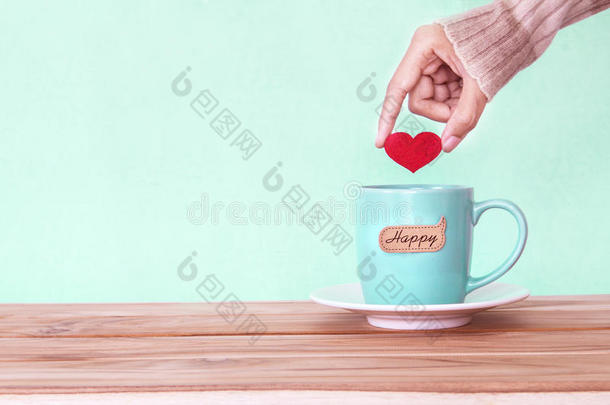 手拿着红色的心形放进一个咖啡杯杯子里