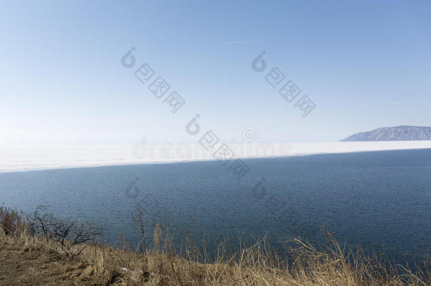 贝加尔湖春景观。 白雪覆盖的湖岸。 岩石森林海岸线。 冰和开放的边界