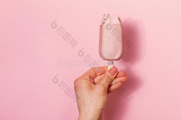 年轻女人的手拿着粉红色背景的冰淇淋。 时尚背景。 夏天的概念。