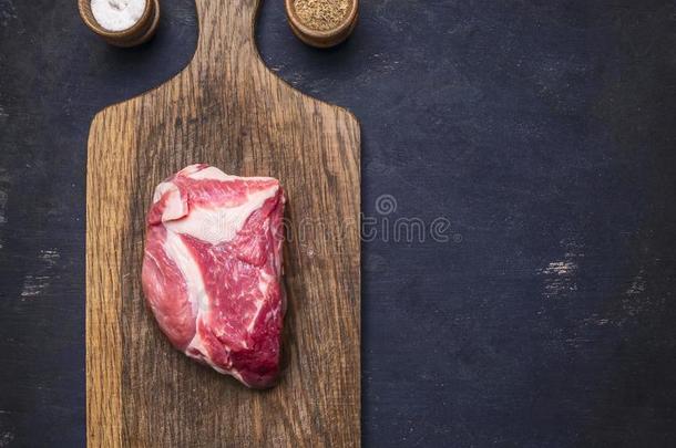 新鲜的生猪肉牛排在老式切割板上，肉在深色的木制背景上，带有胡椒，盐，有文字的空间