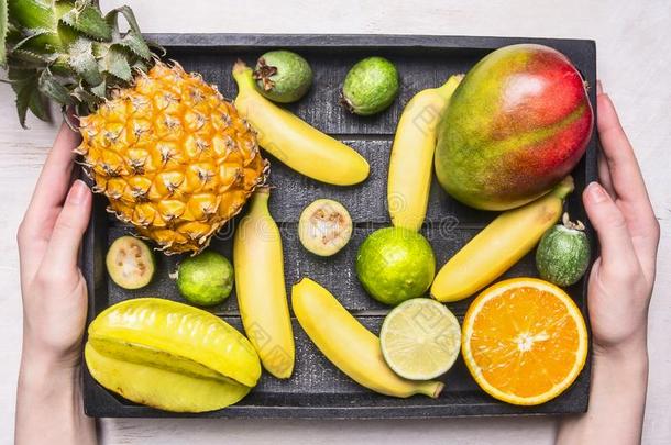 新鲜的夏季水果组合，迷你菠萝，芒果，迷你香蕉，杨桃，石灰，在木箱里，抱着女孩，顶部的景色