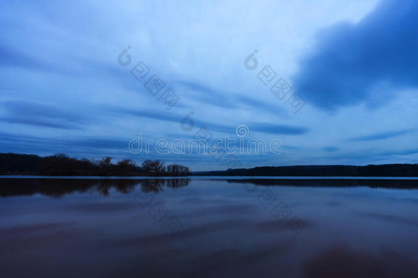 深蓝色和紫色的日落在平静的湖面上，在远处降落