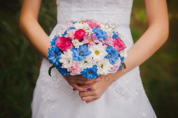美丽的婚礼花束在新娘和新郎的手在公园的背景。 白色和蓝色雏菊婚礼花束