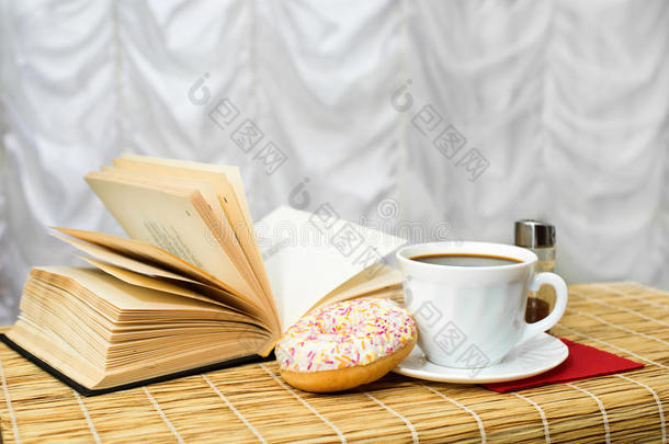 黑<strong>色</strong>咖啡在一个杯子与肉桂，甜甜圈和打开的书