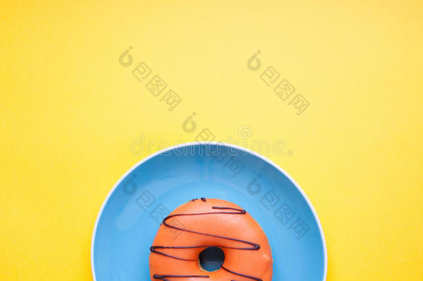 蓝色盘子，在黄色背景上的釉中有橙色甜甜圈。 顶部视图与复制空间。 最小的概念