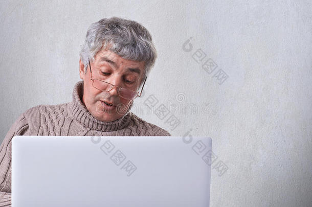一位戴眼镜的老祖父用<strong>笔记本电脑</strong>打电话给他的孩子。 一个使用<strong>笔记本电脑</strong>的孤独的退休者