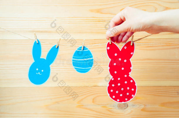 彩色纸兔和纸蛋剪影框架的特写悬挂在木制背景的绳索上。 手挂着爸爸