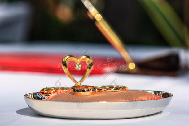 <strong>金色</strong>结婚戒指在人造鱼子酱装饰垫上，心在白色织物上，笔背景在<strong>户外</strong>婚姻登记处