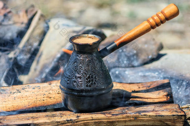黑色咖啡被煮在一个金属CEZVE与一个木制手柄在篝火在早晨关闭风景