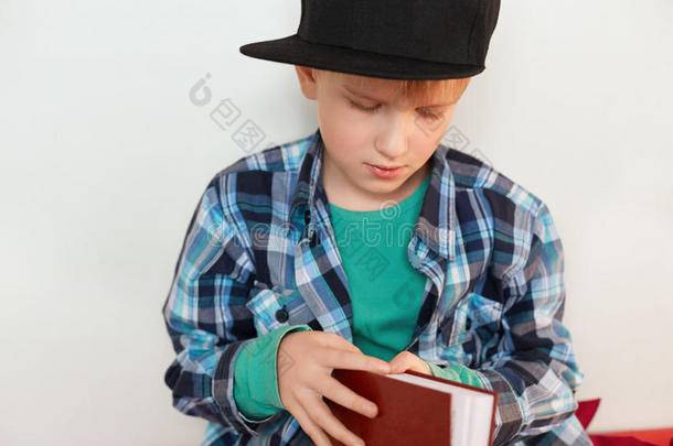 童年和休闲。 学生的形象，在时尚的检查衬衫和帽子打开红色的书孤立在白色背景上想要