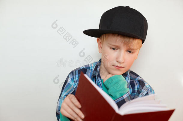 一个小学年龄的孩子在做家庭作业戴着金色头发和蓝色眼睛的帽子的男孩拿着一本书看书做作业