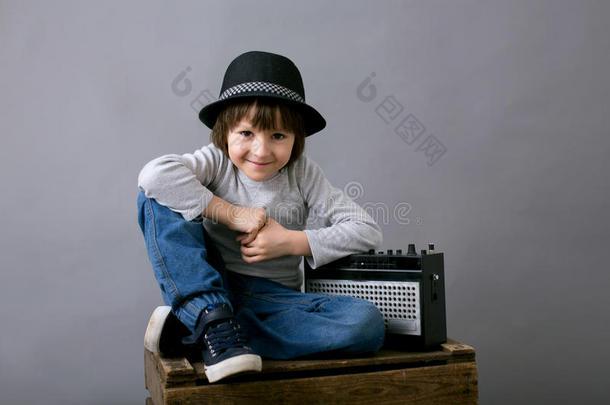 可爱的男孩戴着黑色的帽子，坐在木制托盘上，拿着收音机