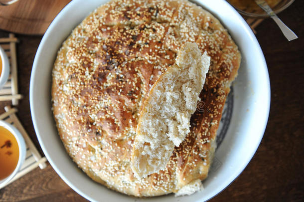 新鲜的圆形Focaccia面包与芝麻陶瓷形式与面包关闭。 草药茶，杯子，果酱