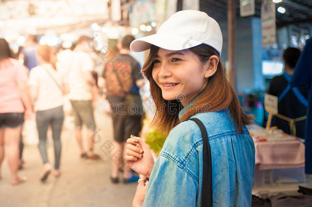 一位戴着帽子的年轻女子正在泰国一个亚洲国家的市场街道上行走