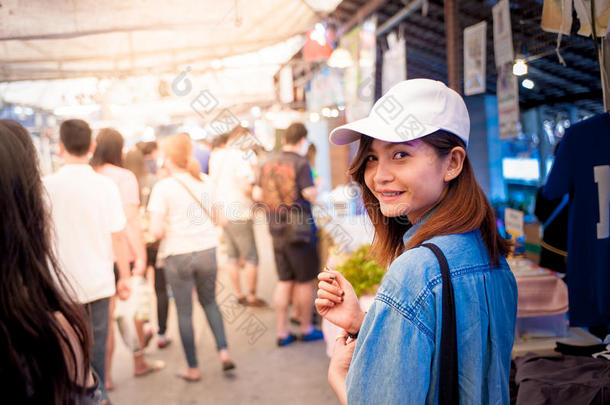 一位戴着帽子的年轻女子正在泰国一个亚洲国家的市场<strong>街道</strong>上<strong>行走</strong>