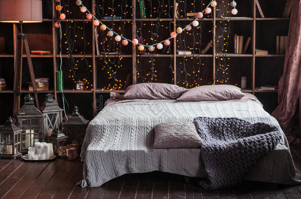 舒适，舒适，室内和假日概念-舒适的卧室与床和花环灯在家里。 有书的架子
