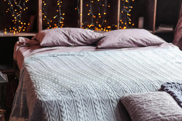 舒适，舒适，室内和假日概念-舒适的卧室与床和花环灯在家里。 有书的架子