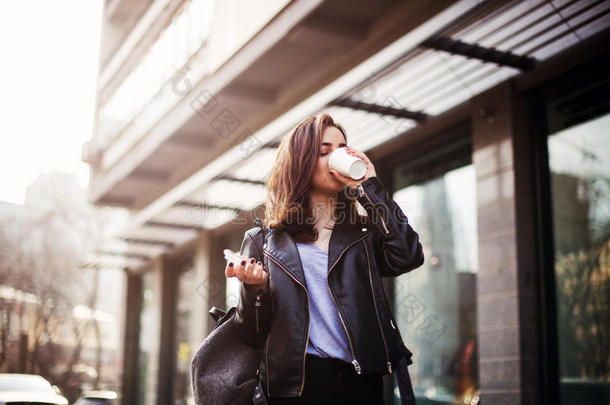 特写时尚<strong>街头风</strong>格的肖像，一个穿着休闲服装的漂亮女孩在城市里散步。 漂亮的黑发女人喝咖啡