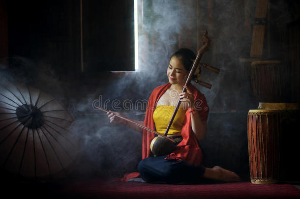 穿着传统服装的漂亮女人玩高音小提琴。 高音小提琴或女高音演奏泰国弦乐器