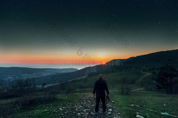 一个年轻人站在山顶上享受日落和星空