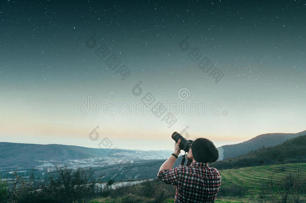 一个年轻人在日落时站在山顶上拍摄星空