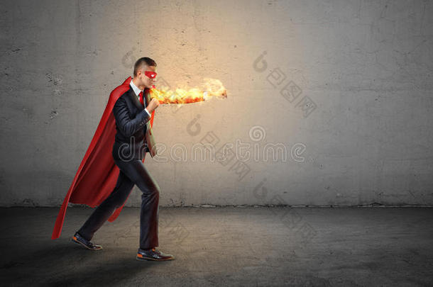 一个穿着红色超级<strong>英雄</strong>斗篷的商人和一只燃烧的手在混凝土背景上向一个看不<strong>见</strong>的敌人挥拳。